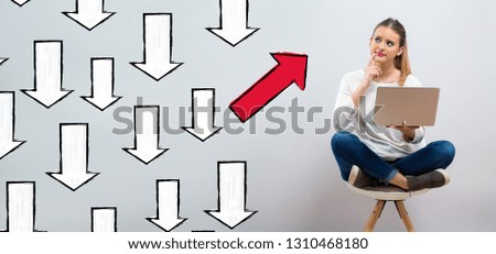 Arrow going in a different direction with young woman using her laptop on a grey background
