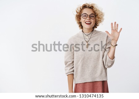 Hello my name is. Portrait of friendly-looking outgoing and relaxed carefree attractive hipster girl with glasses and sweater raising palm to wave hi and greet new members of group smiling joyfully