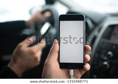 Close-up, hand of man holding smartphone with mockup on background of car dashboard.