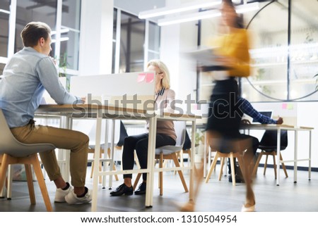 Work lifestyle in modern office: busy people working at tables in open space office, blurred motion of business lady