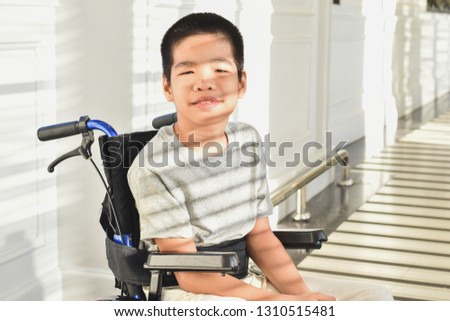 Child on wheelchair is smiling, his face has  light and shadow . Happy disabled child concept.