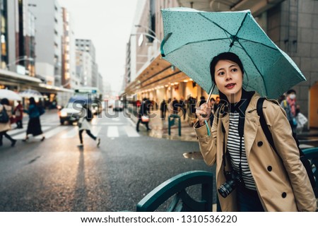 backpacker photographer holding umbrella walking in busy city urban kyoto japan in rainy day. Woman going on street during rain bad weather travel in asia. elegant tourist with camera sightseeing.