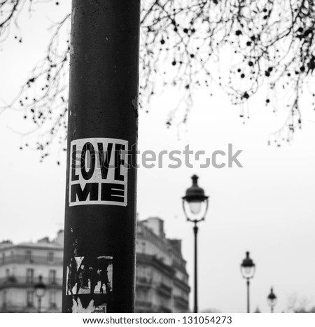 LOVE ME sticker on streetlight.  Parisian street at background. Retro style postcard. 