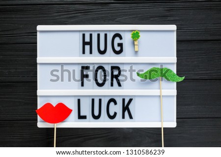 Lightbox with title Hug for luck and photobooth  bow tie lips on wooden sticks at black wooden background. Creative background to St. Patricks Day