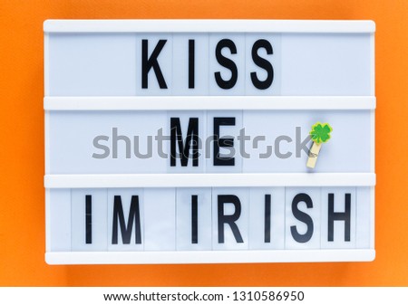 Lightbox with title Kiss me i'm Irish and photobooth lips on wooden sticks at orange background. Creative background to St. Patricks Day