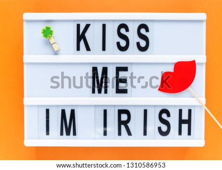 Lightbox with title Kiss me i'm Irish and photobooth lips on wooden sticks at orange background. Creative background to St. Patricks Day
