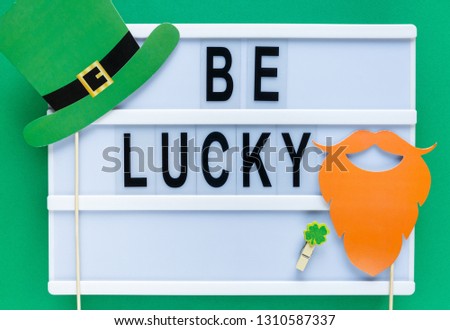 Lightbox with title Be lucky and photobooth bow tie hat beard on wooden sticks at green background. Creative background to St. Patricks Day