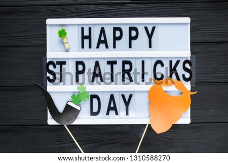 Lightbox with title Happy st Patrick Day and photobooth bow tie beard on wooden sticks on black wooden background. Creative background to St. Patricks Day