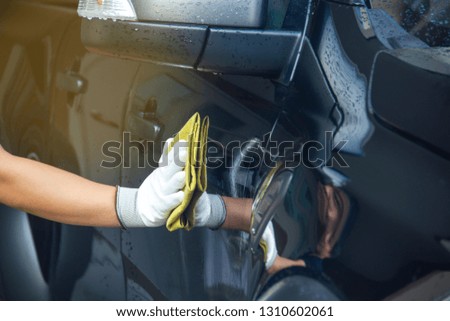 This image is a picture of wiping the car by a yellow microfiber cloth with hand wearing gloves.Car wash concept.