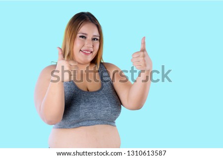 Picture of pretty fat woman smiling at the camera while showing thumbs up in the studio
