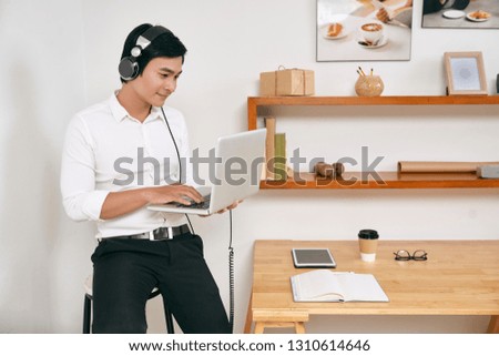 Creative young Asian man wearing headphones when working on laptop in his office