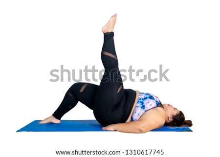 Picture of young obese woman lifting her leg while doing yoga exercise in the studio, isolated on white background