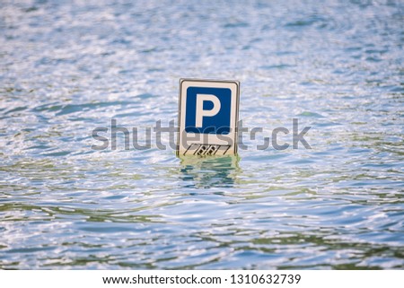 Parking road sign partially submerged in a flood. Letter P indicating parking for cars. Flooding due to very strong climatic perturbations. Location: Italy