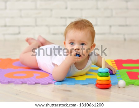 A 7-month-old baby plays on the floor with toys and stuffs small parts into his mouth. Security concept Royalty-Free Stock Photo #1310661200