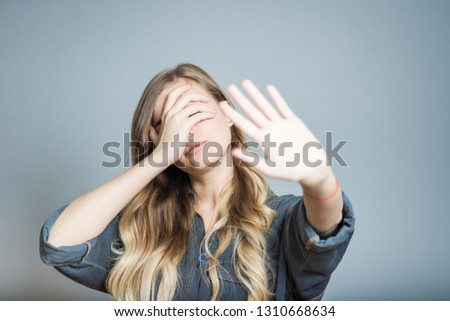 Beautiful blonde girl hides her face with hands, isolated on gray background