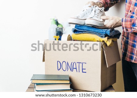 CLOTHES DONATION AND FOOD DONATION CONCEPT. A man holding a donation box with clothes, shoes and hygiene products. Copy space