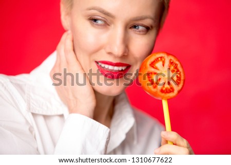 Portrait of beautiful caucasian woman eating tomato over red wall background