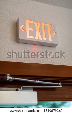 Red and white exit sign above a door way