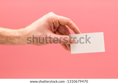 Hand holding a blank white business card in front of a pink background