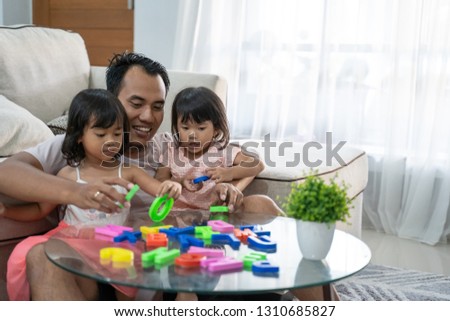 portrait of togetherness father and his two daughters playing colorful alphabet text in the living room