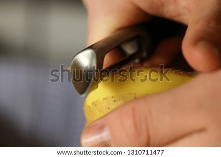 A man peeling a potato with metallic potato peeler. You can see hands, one potato and the peeler in this photo. Color image. Closeup photo with macro lens.