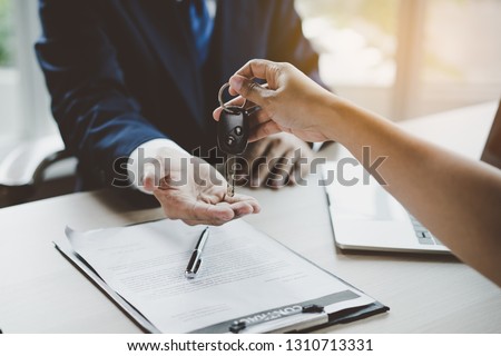 Car rental service concept. Close up view Hand of agent giving car key to customer after signed rental contract form. Royalty-Free Stock Photo #1310713331