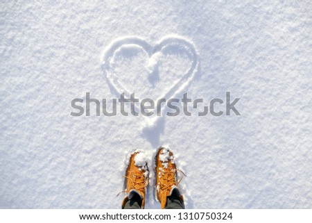 Top view of yellow shoes / boots footprint in fresh snow. Winter season. Looking at the drawn heart in the snow. Valentines day. Royalty-Free Stock Photo #1310750324