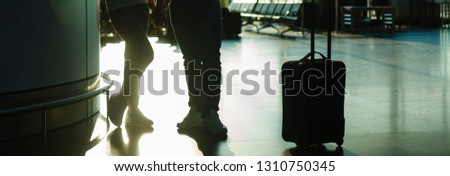 Young couple with suitcases are looking through airport window while waiting for flight. Back view.