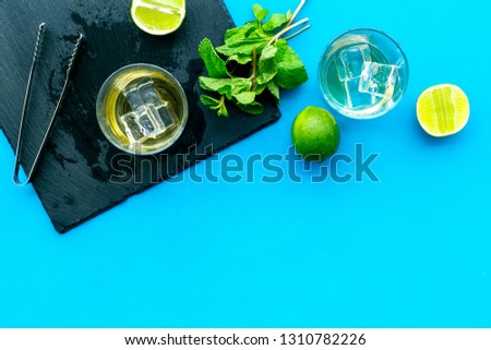 Alcoholic beverage. Whiskey with ice, mint and lime on black board on blue background top view space for text