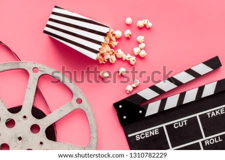 Movie premiere concept. Clapperboard, film stock, popcorn on pink background top view