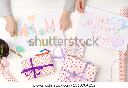 Happy mother's day card made by little child. Girl's hands holding a handmade cards with giftboxes.