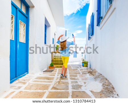 Little tourist girl in white hat takes a picture of typacal greek street on a holiday