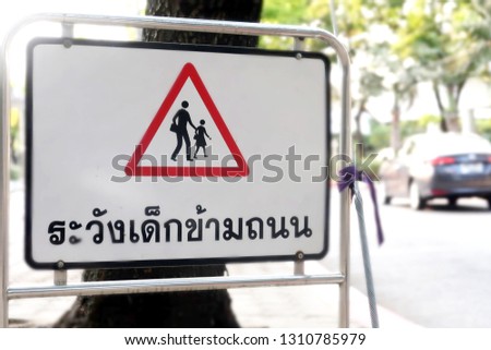 A symbol roadside sign (Thai text translation is Be careful to children)  on the road in front of school.