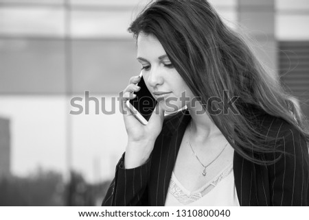 Beautiful young happy business woman with phone against the background of the glass building. Black and white photography.