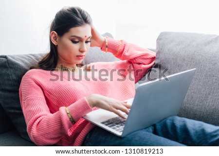 beautiful indian woman with bindi using laptop on sofa