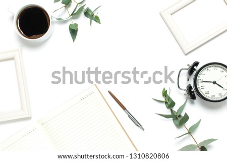 Flat lay cup of black coffee, black alarm clock, notebook, diary, eucalyptus on white background top view copy space. Minimalistic food concept, Feminine desk workspace, time to work coffee background