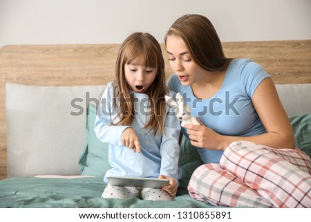 Mother and little daughter with tablet computer on bed