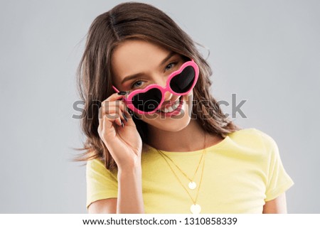 summer, valentine's day and people concept - smiling young woman or teenage girl in yellow t-shirt and heart-shaped sunglasses over grey background