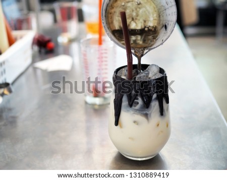A glass of iced dark cocoa; upper layer is black cocoa lower is fresh milk decorated with melted black cocoa, blur background with selective focus.
