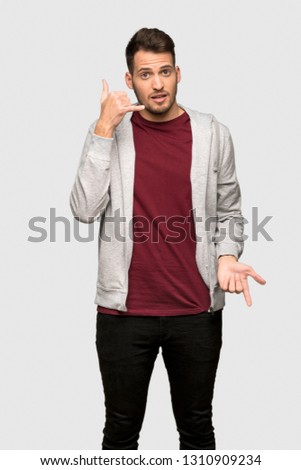 Man with sweatshirt making phone gesture and doubting over grey background