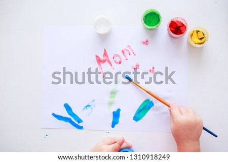 Baby painting picture for mother. Mother's day picture. Baby hands. Baby fingers in paint. Baby holds the brush. White paper. 