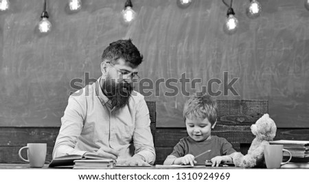 Teacher with stylish mustache and beard and small kid writing letters in copybook. Cute boy drawing a picture with colorful pencils. Art lesson at kindergarten.