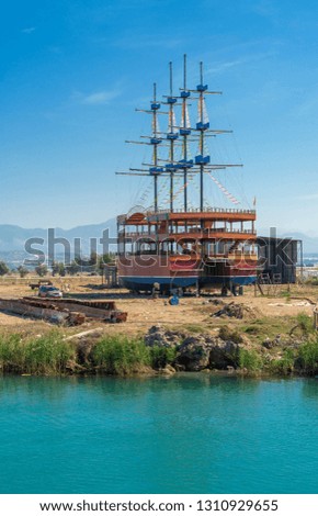 A large sailing ship in a pirate style is moored on the shore for repair against a blue sky. Photos of ship from sea. The concept of summer holidays, sports, tourism 