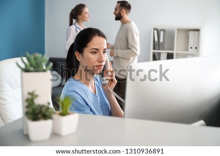 Female receptionist talking by phone in clinic Royalty-Free Stock Photo #1310936891