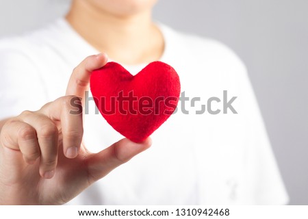 Woman's hand with white t-shirt holding red fabric heart shaped 