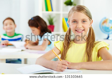Portrait of lovely girl looking at camera at workplace with schoolmates on background