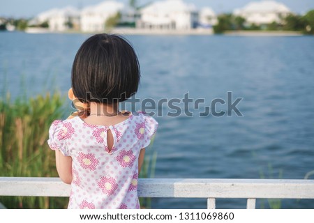 A portrait photo of a one happy girl standing by lake. She is holding cute little teddy bear in her hands. Cute child concept. 