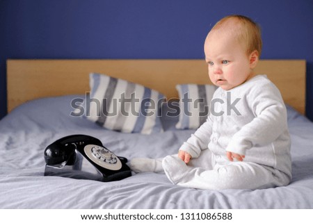 Small cute baby on a comfy bed using an old fashioned style phone, listening to a phone call explaining Brexit.