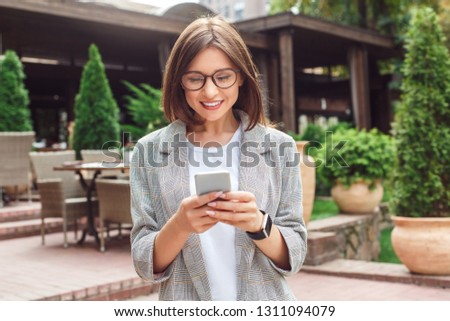Young businesswoman wearing eyeglasses standing on the city street using application on smartphone smiling happy