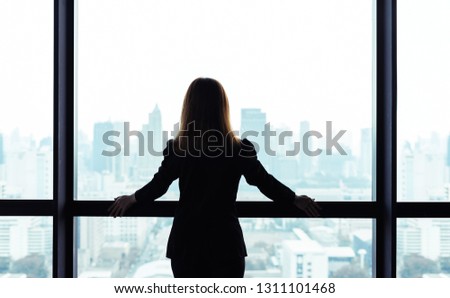Asian business woman standing and looking out the window at city view background Royalty-Free Stock Photo #1311101468